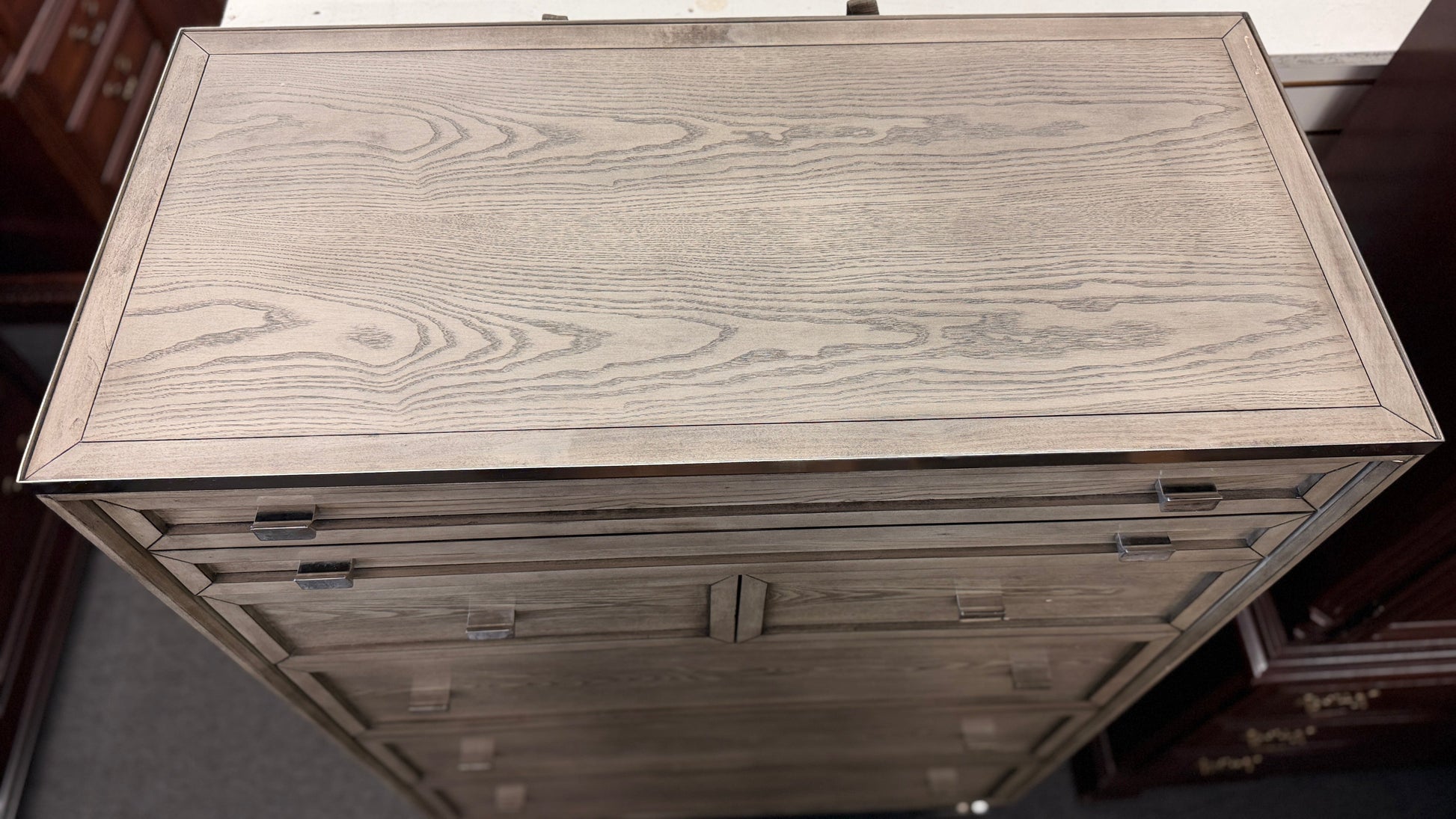 A contemporary tall 7-drawer highboy chest of drawers with a soft gray-washed wood grain finish, minimalist silver hardware, and a geometric chrome base.