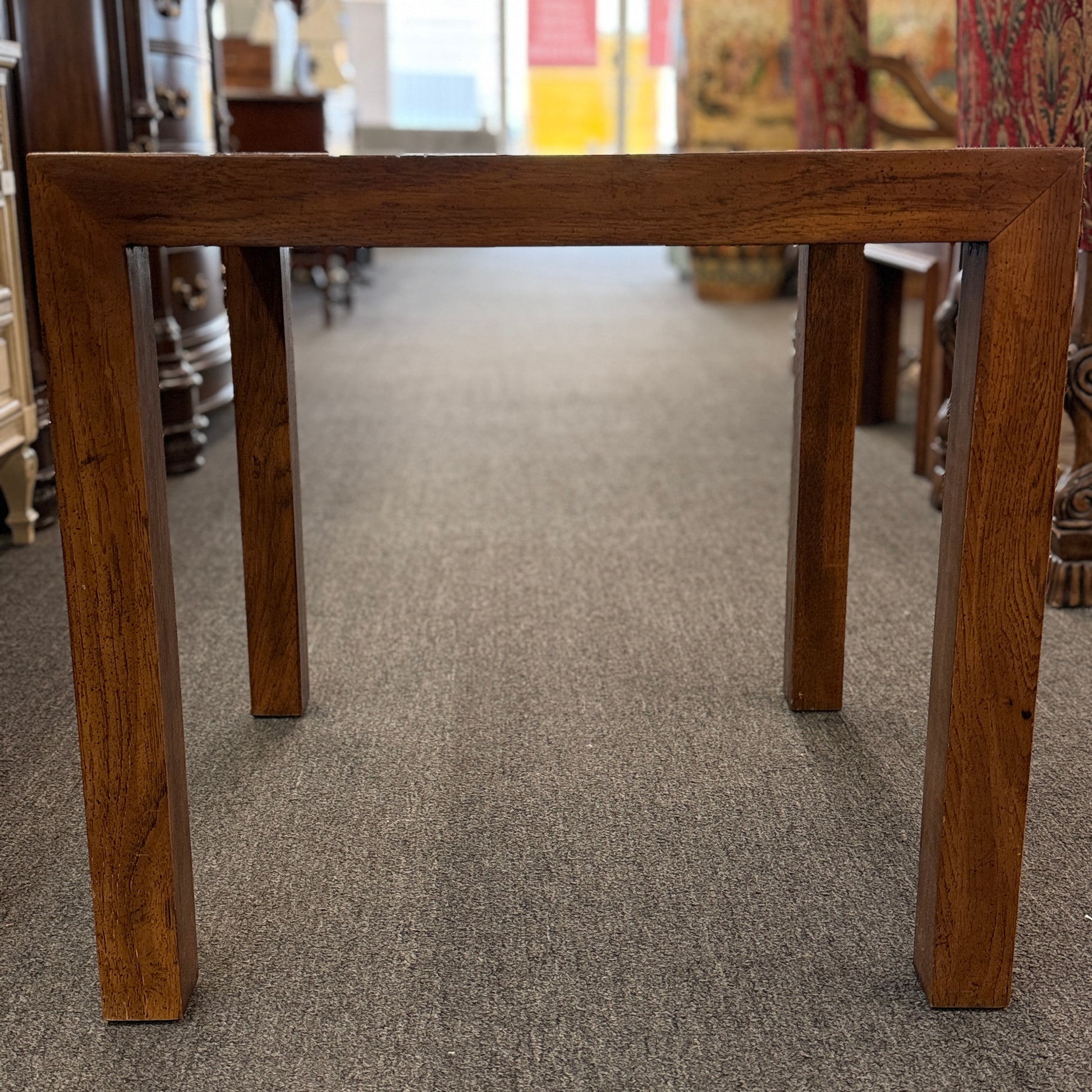 A modern square accent table with thick blocky legs flush with the corners and a highly reflective, glossy top surface showing a rich burl wood pattern.