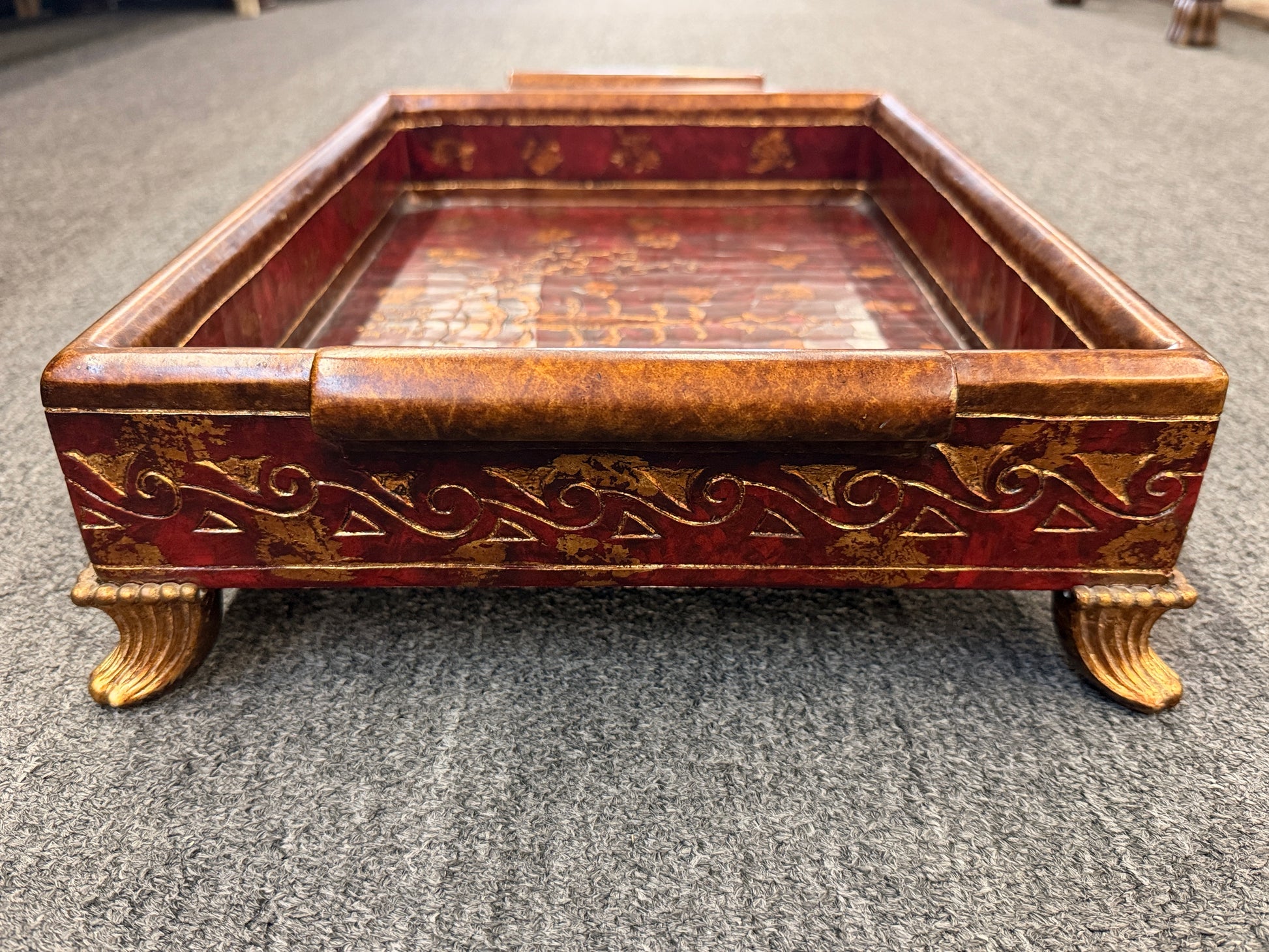 A rectangular wooden decorative vanity tray with ornate gold wave patterns on the sides, handles, short feet, and a faux-tortoiseshell interior with gold botanical designs.