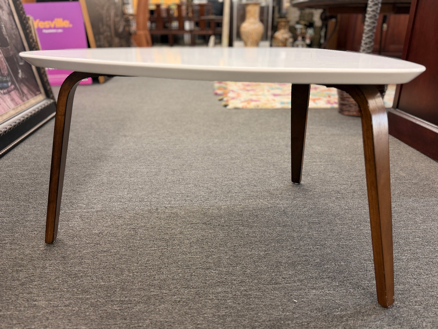 A retro-inspired triangular end table featuring a smooth white guitar-pick-shaped top supported by three splayed, tapered dark wood legs.