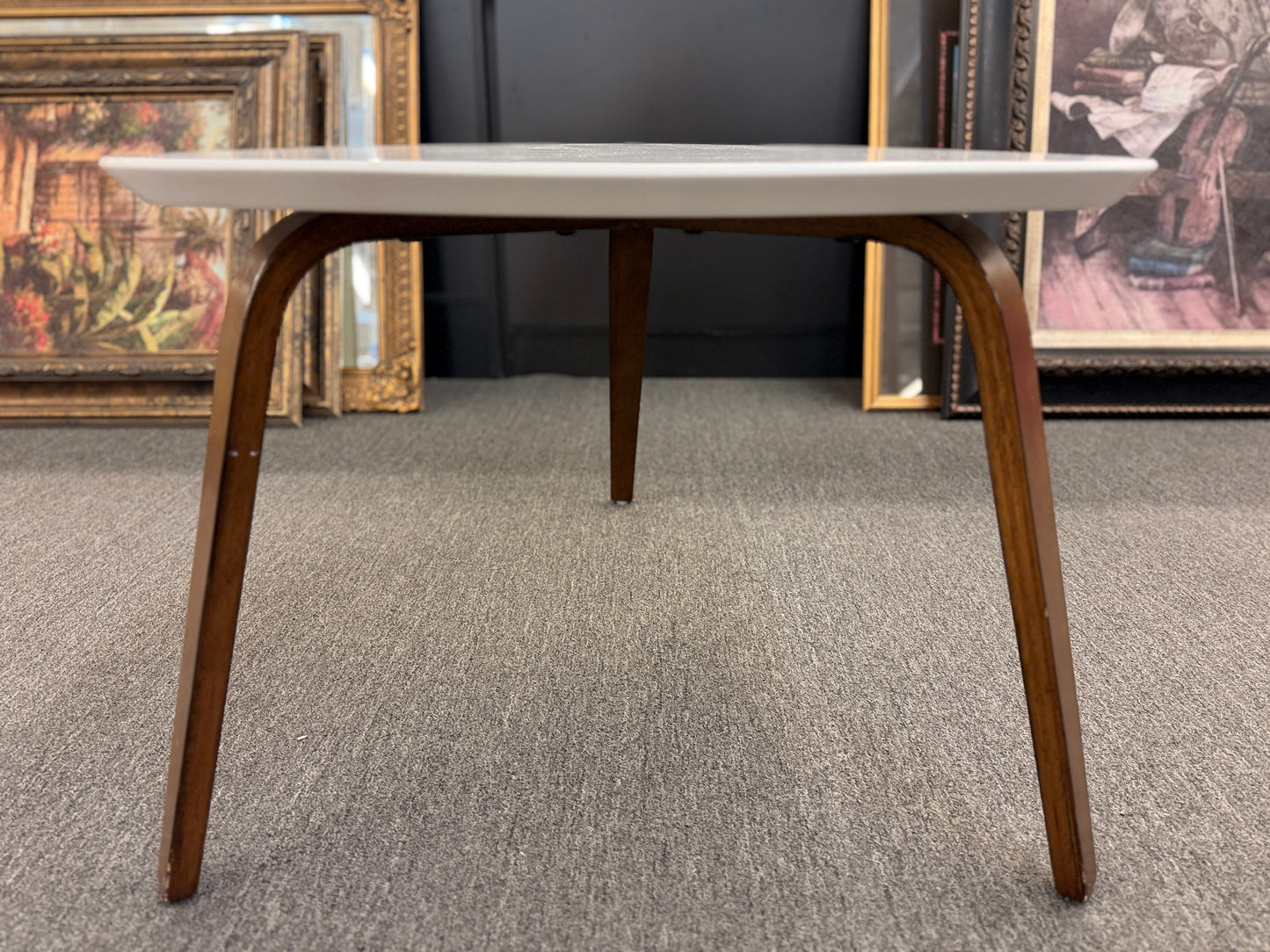 A retro-inspired triangular end table featuring a smooth white guitar-pick-shaped top supported by three splayed, tapered dark wood legs.