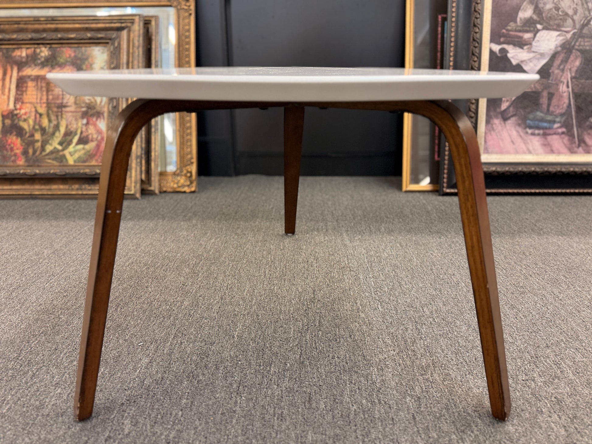 A retro-inspired triangular end table featuring a smooth white guitar-pick-shaped top supported by three splayed, tapered dark wood legs.