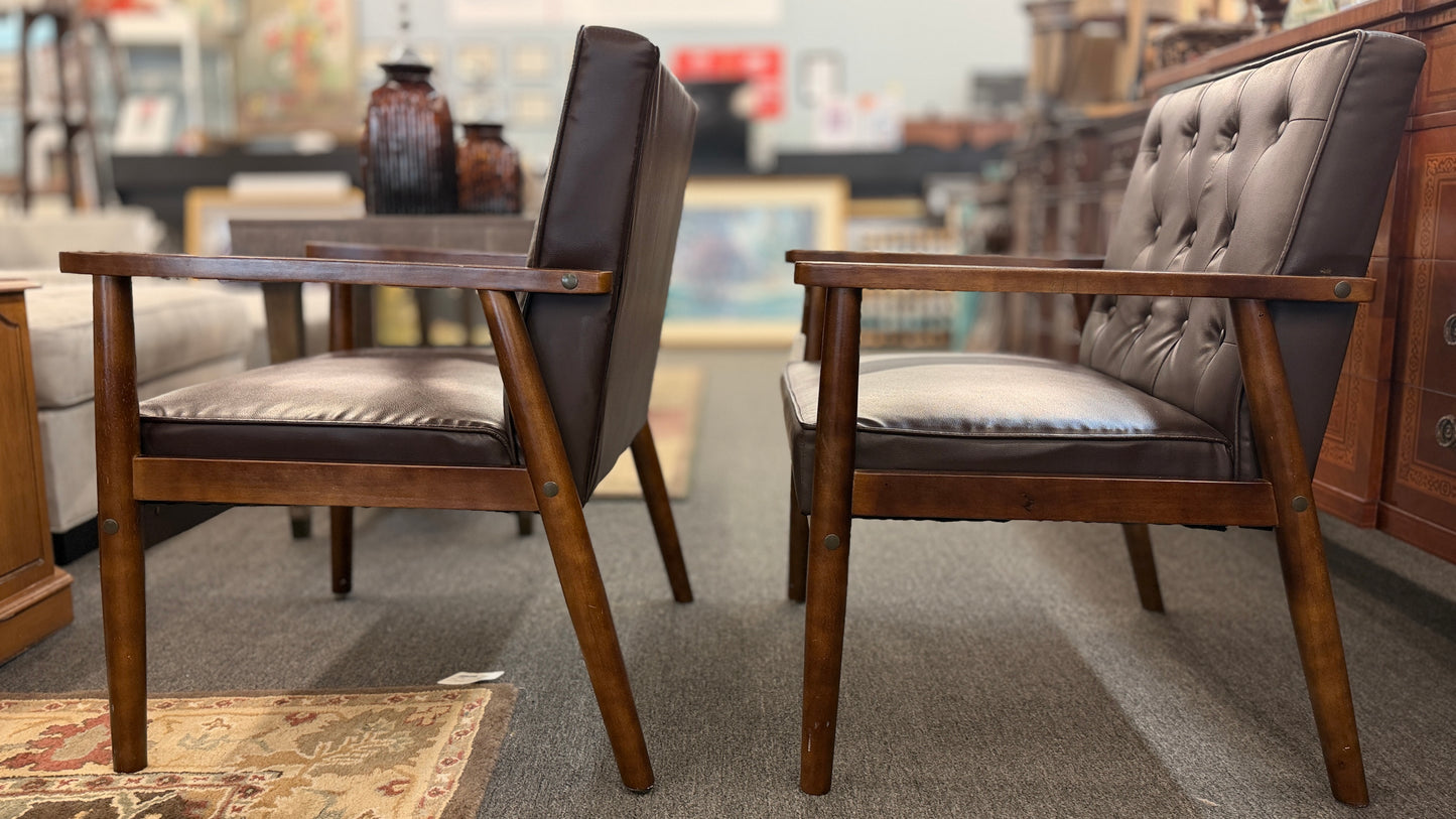 A pair of mid-century modern style accent armchairs featuring dark brown button-tufted backrests, smooth seat cushions, and exposed medium-toned wooden frames with tapered legs.