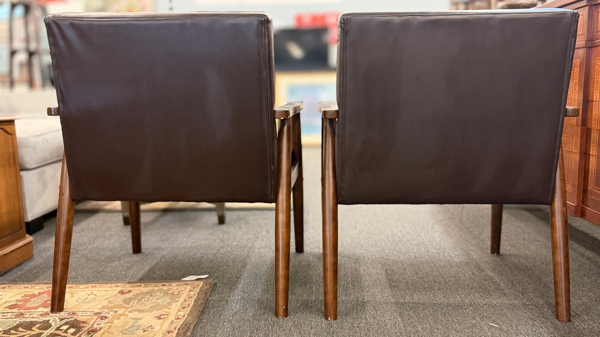 A pair of mid-century modern style accent armchairs featuring dark brown button-tufted backrests, smooth seat cushions, and exposed medium-toned wooden frames with tapered legs.