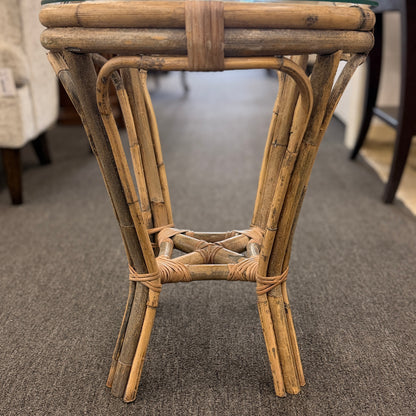 A small round end table with a bent organic-style bamboo frame, wrapped structural joints, an X-shaped cross-stretcher, and a clear glass tabletop.