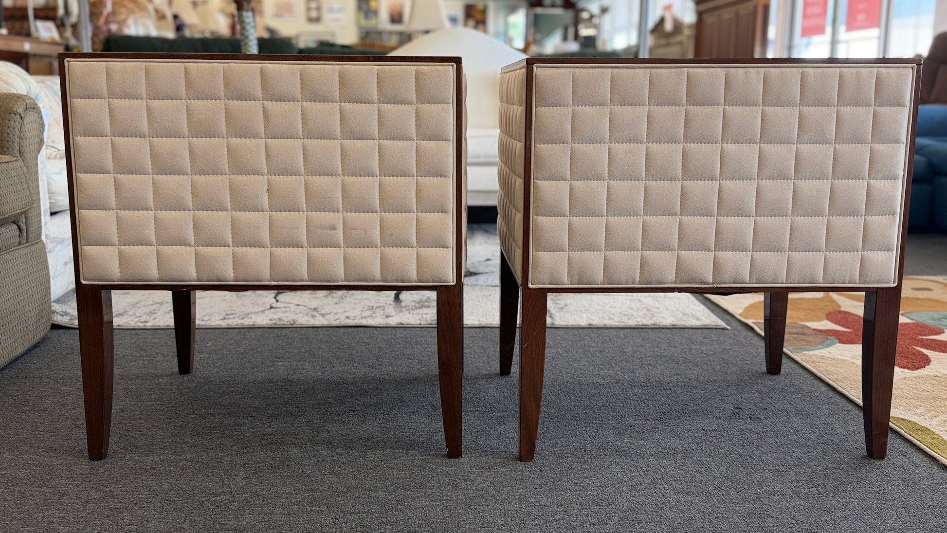 A pair of contemporary squared-off accent chairs with light beige suede-like upholstery, an exposed dark wood outer frame, and subtle quilted tufting on the side panels.