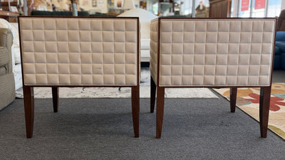 A pair of contemporary squared-off accent chairs with light beige suede-like upholstery, an exposed dark wood outer frame, and subtle quilted tufting on the side panels.