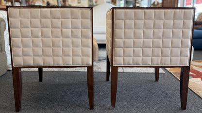 A pair of contemporary squared-off accent chairs with light beige suede-like upholstery, an exposed dark wood outer frame, and subtle quilted tufting on the side panels.