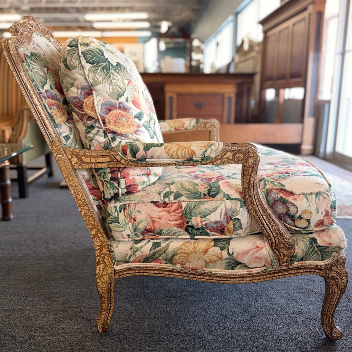 A French provincial-style armchair with an intricately carved exposed wooden frame, elegant cabriole legs, and vibrant multicolored floral fabric upholstery.