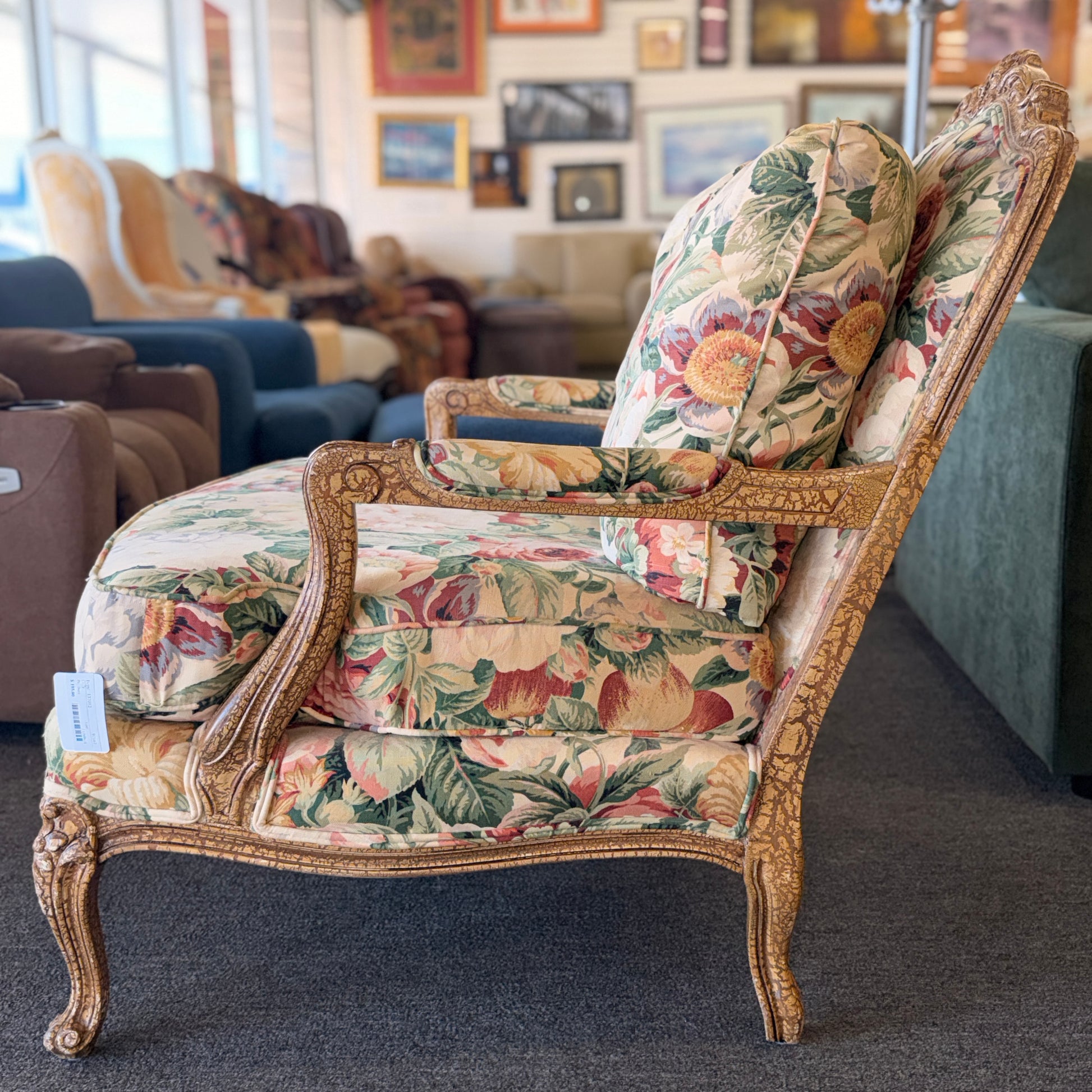 A French provincial-style armchair with an intricately carved exposed wooden frame, elegant cabriole legs, and vibrant multicolored floral fabric upholstery.