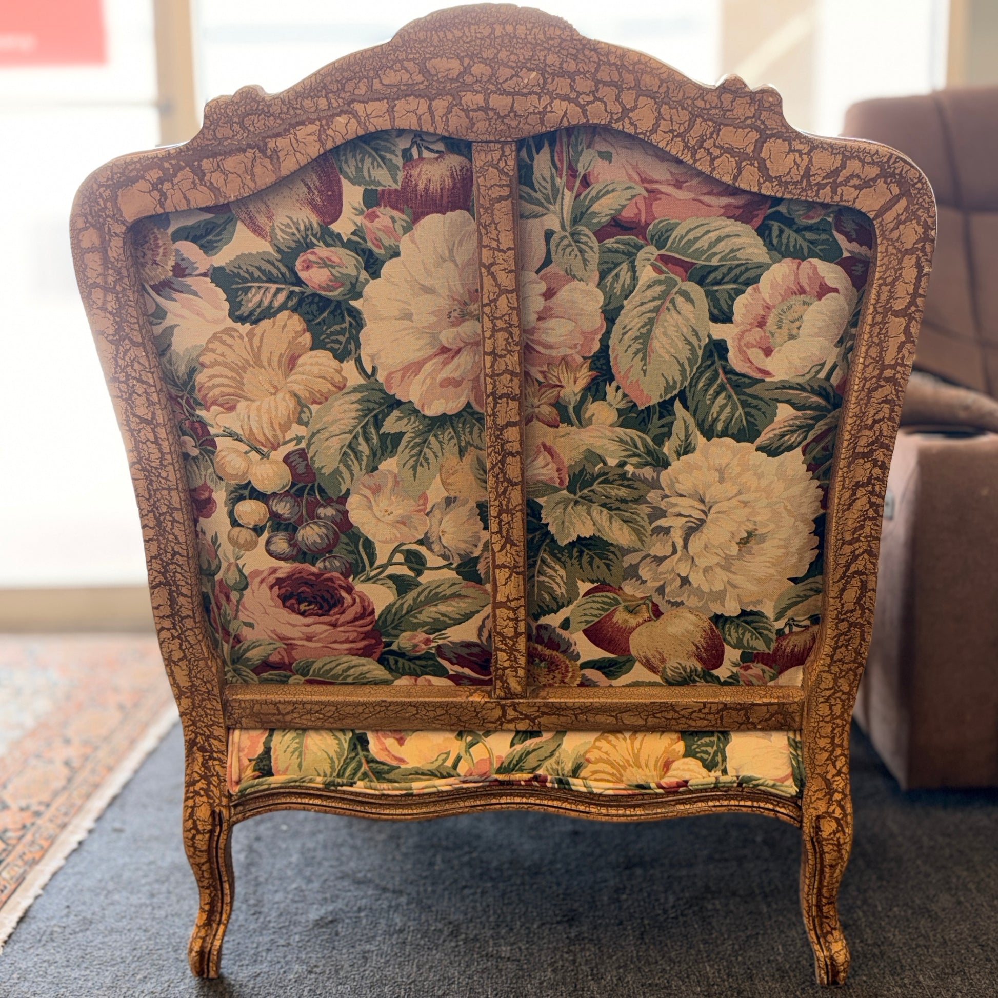 A French provincial-style armchair with an intricately carved exposed wooden frame, elegant cabriole legs, and vibrant multicolored floral fabric upholstery.
