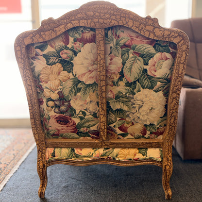 A French provincial-style armchair with an intricately carved exposed wooden frame, elegant cabriole legs, and vibrant multicolored floral fabric upholstery.