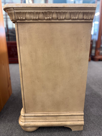 A traditional antique-style nightstand featuring a solid marble top, three serpentine-front drawers, fluted side pilasters, and an antiqued distressed painted finish.