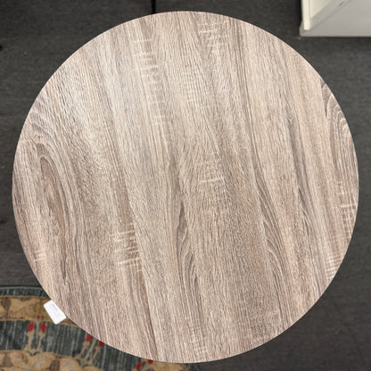 Round pub table with a light brownish-grey faux wood grain top and a dark metal pedestal base featuring curved intersecting legs.