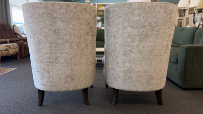 Matching pair of transitional wingback accent armchairs upholstered in textured light beige fabric with dark brown tapered wooden legs.