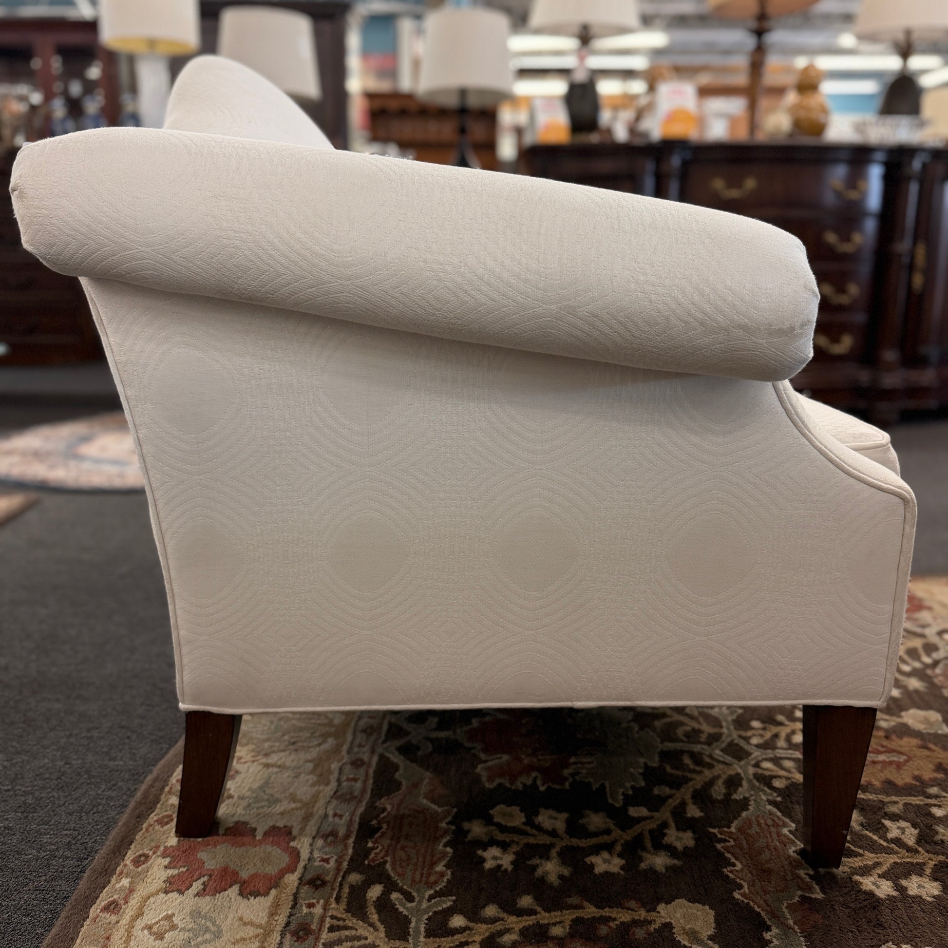 Cream upholstered Ethan Allen camelback loveseat featuring rolled arms, a single seat cushion, two matching throw pillows, and dark tapered wooden legs.