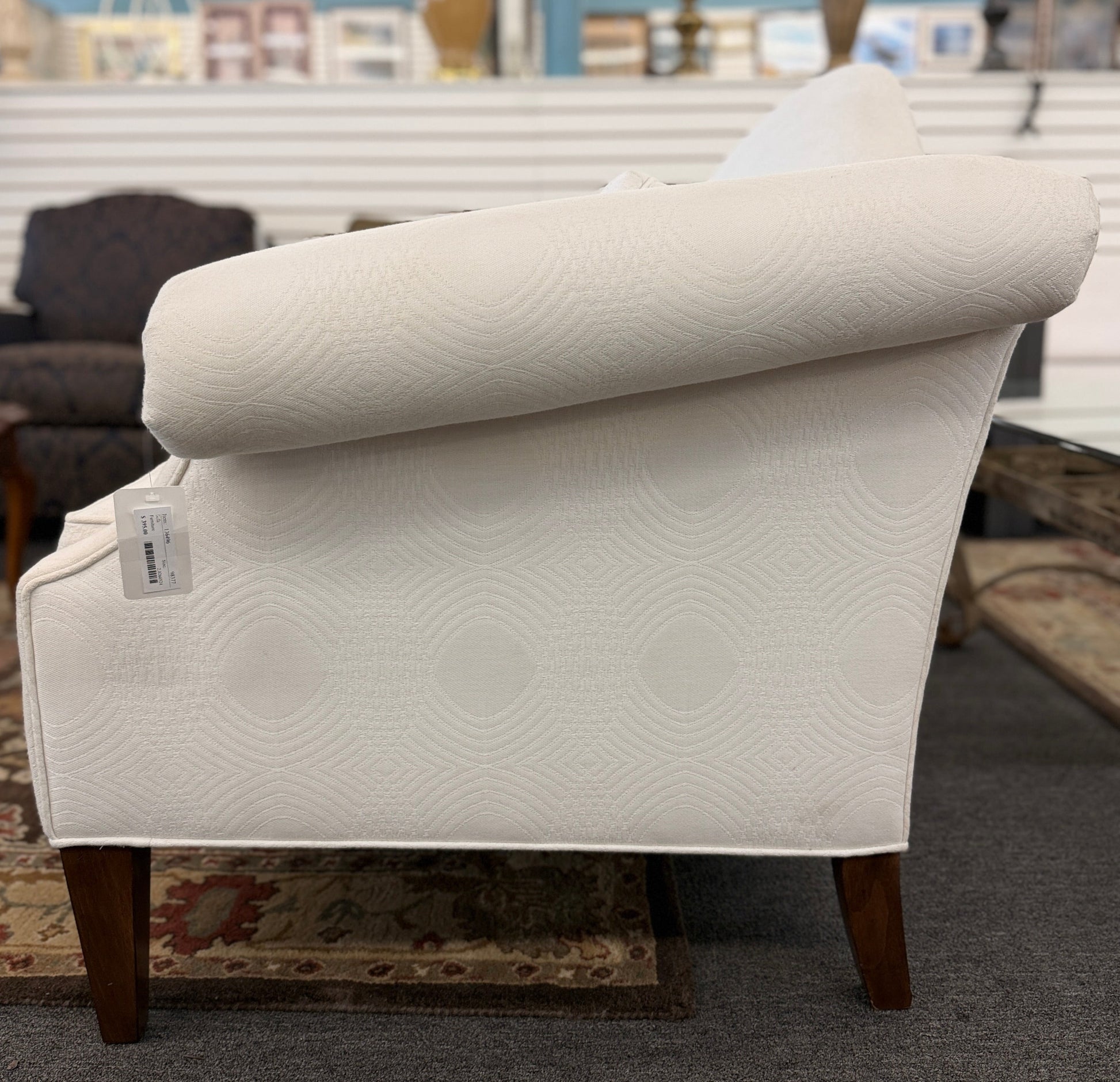 Cream upholstered Ethan Allen camelback loveseat featuring rolled arms, a single seat cushion, two matching throw pillows, and dark tapered wooden legs.