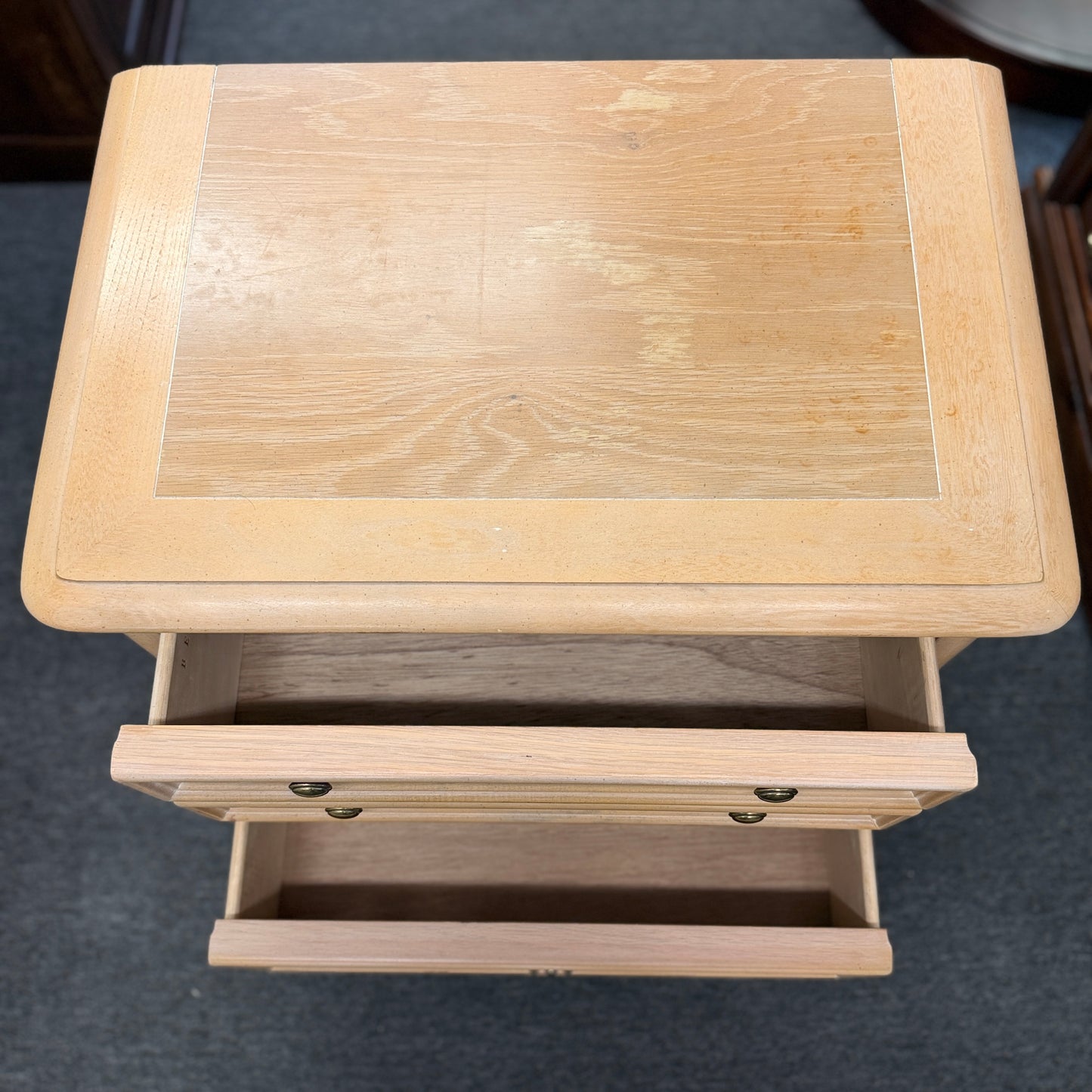 Bernhardt three-drawer wood nightstand with a light finish, routed drawer details, brass knobs, a brass bail pull, and a scalloped base.