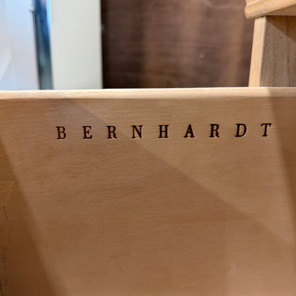 Bernhardt three-drawer wood nightstand with a light finish, routed drawer details, brass knobs, a brass bail pull, and a scalloped base.