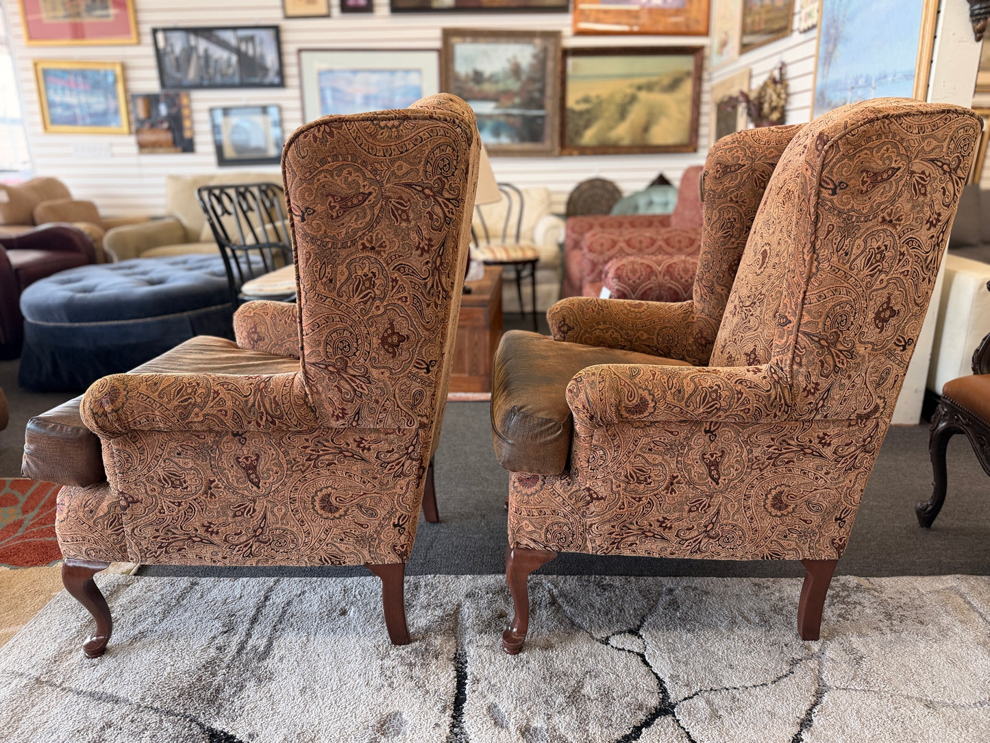 Pair of traditional wingback accent chairs upholstered in tan and brown paisley fabric with curved Queen Anne-style wooden legs.