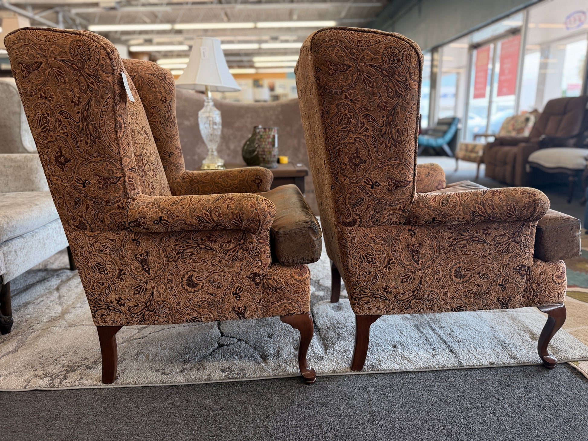 Pair of traditional wingback accent chairs upholstered in tan and brown paisley fabric with curved Queen Anne-style wooden legs.