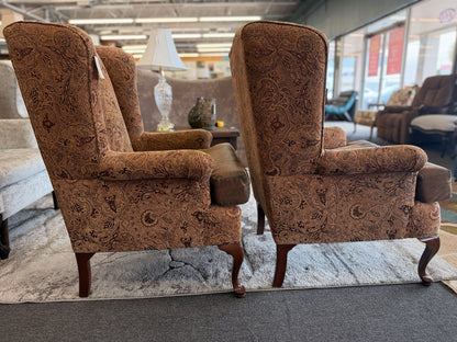Pair of traditional wingback accent chairs upholstered in tan and brown paisley fabric with curved Queen Anne-style wooden legs.