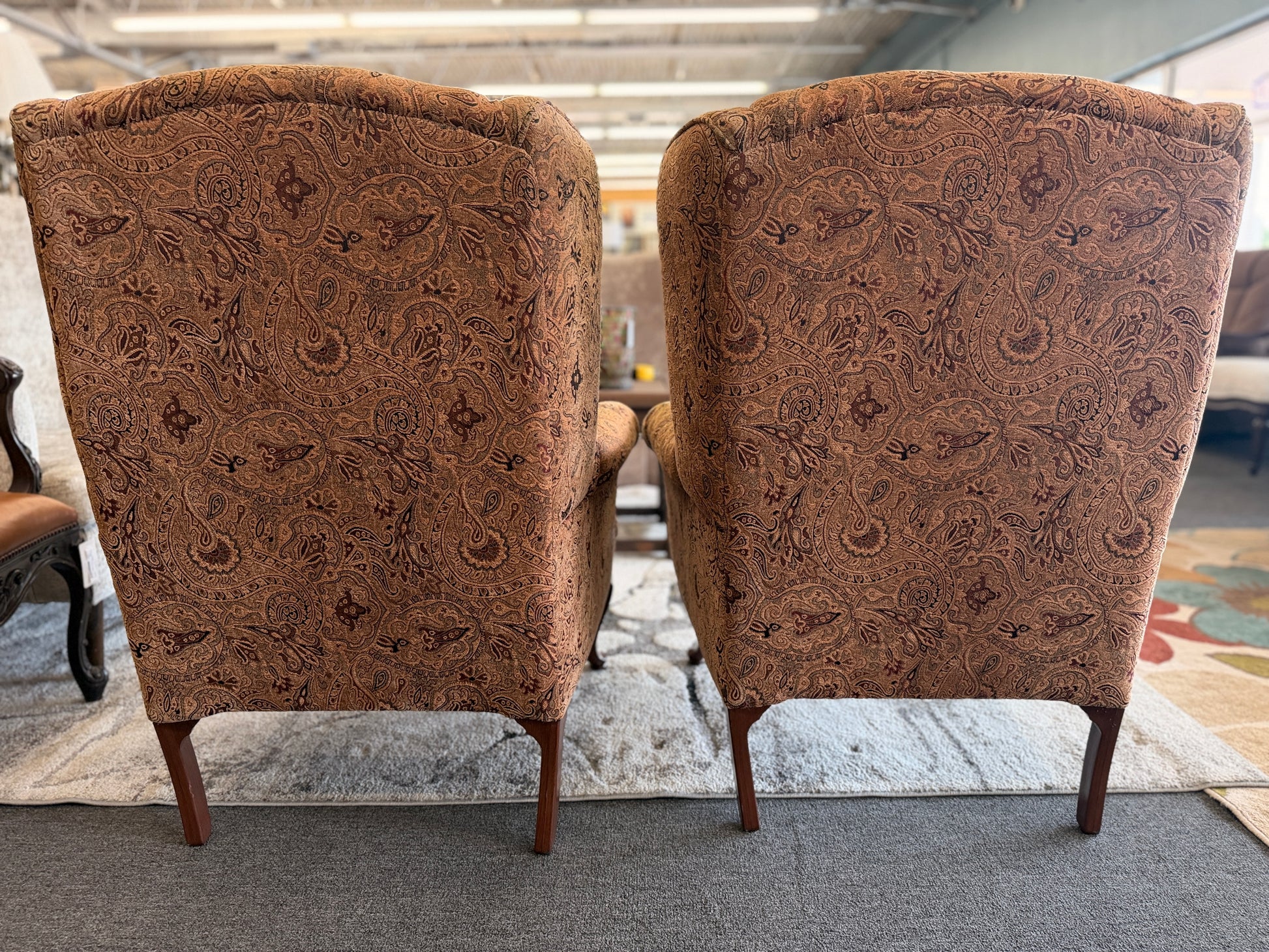 Pair of traditional wingback accent chairs upholstered in tan and brown paisley fabric with curved Queen Anne-style wooden legs.