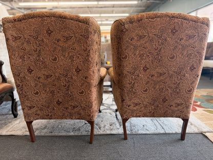 Pair of traditional wingback accent chairs upholstered in tan and brown paisley fabric with curved Queen Anne-style wooden legs.