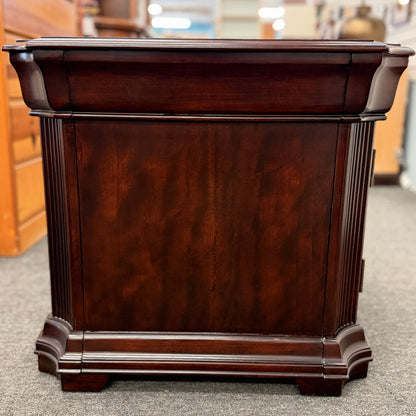 Traditional dark wood nightstand featuring a top drawer, lower cabinet door, fluted corner details, and a classic timeless design.