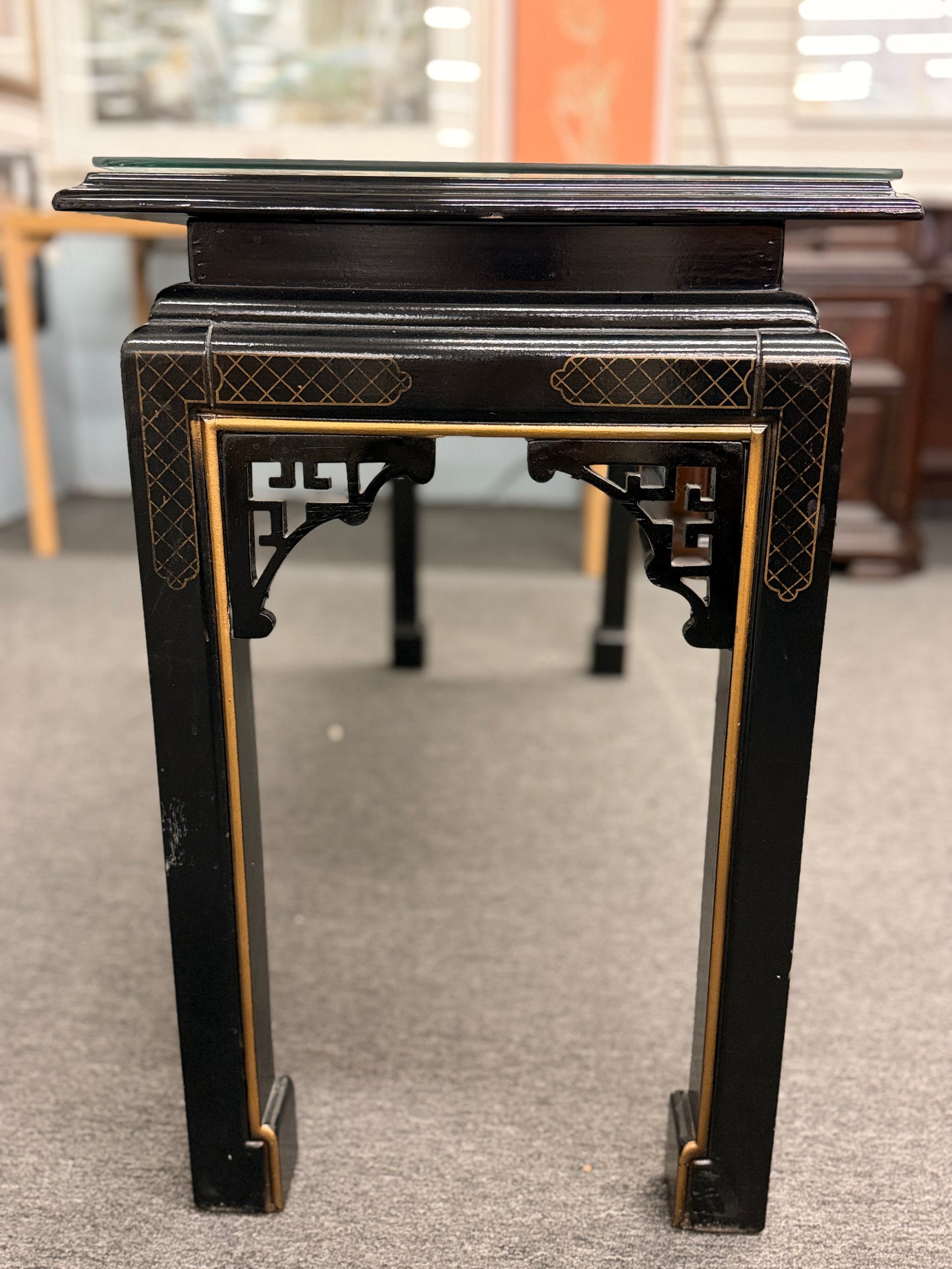 Black lacquer console table featuring hand-painted Asian-inspired scenes with figures, architecture, and landscapes beneath a protective clear glass surface.