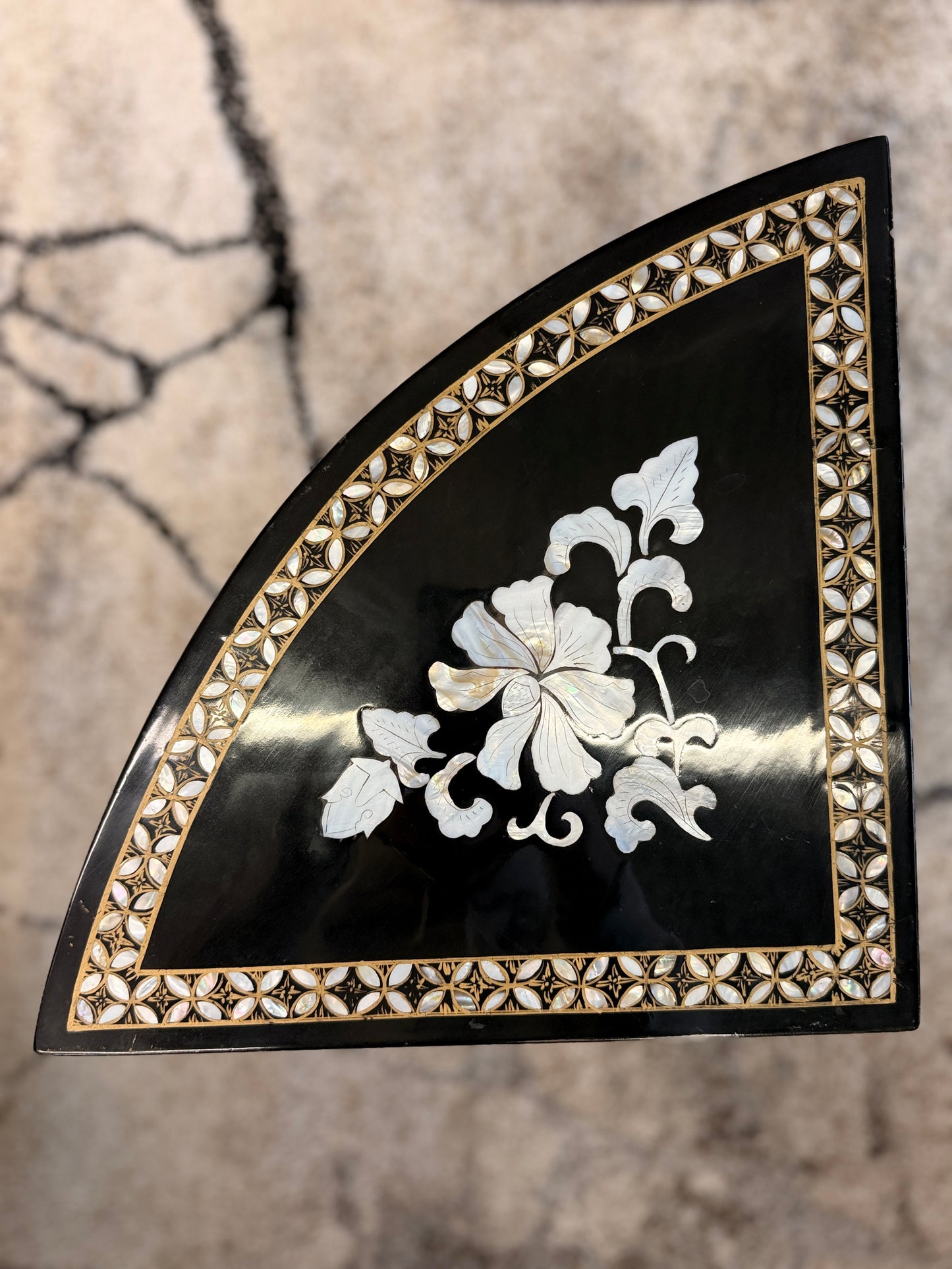 Traditional black lacquer tea table set featuring a round coffee table with a protective glass top, four triangular nesting stools, gold-painted detailing, and mother-of-pearl style floral inlays.