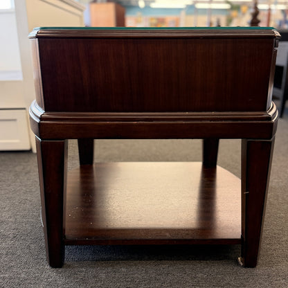 Dark wood nightstand featuring a glass insert top, a single drawer with a silver ring pull, and an open lower display shelf.