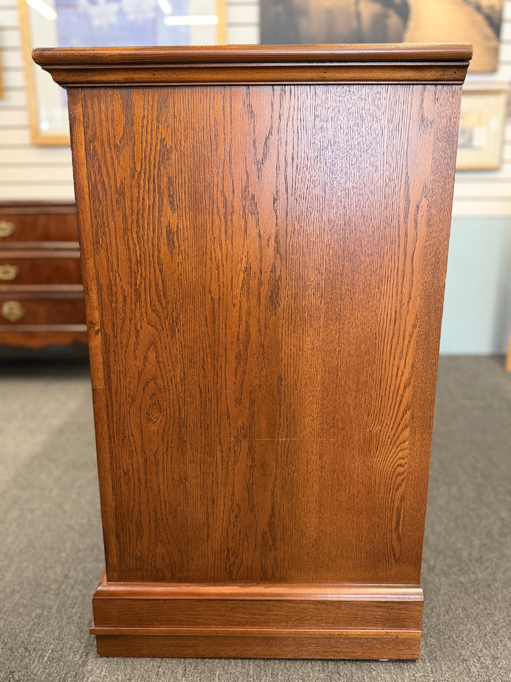 Medium-tone wood storage cabinet featuring three stacked drawers, a glass-paneled cabinet door with interior shelving, and a classic versatile design.