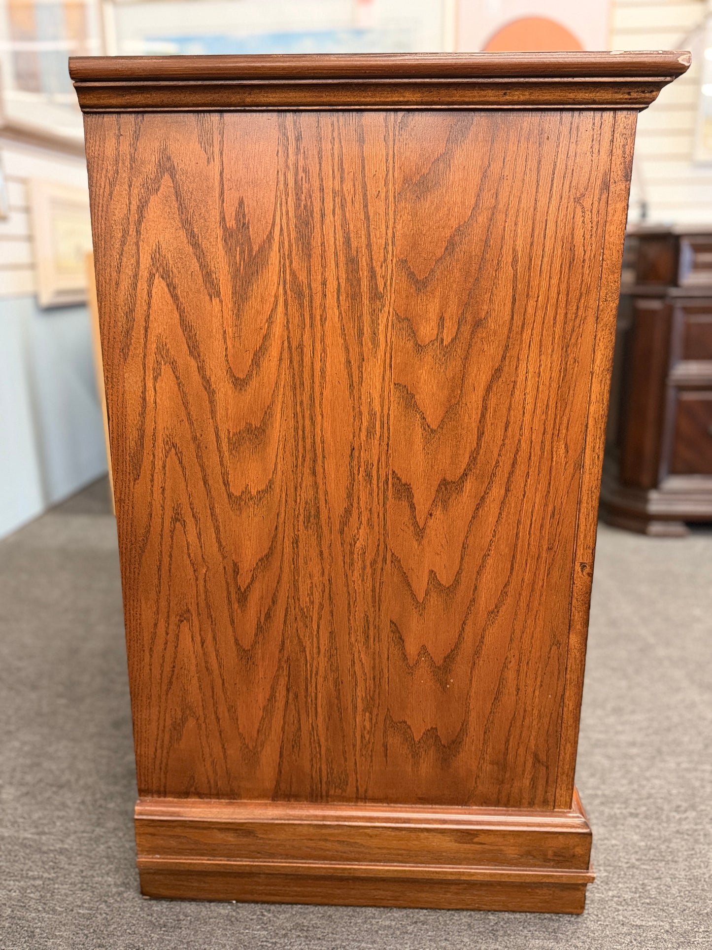 Medium-tone wood storage cabinet featuring three stacked drawers, a glass-paneled cabinet door with interior shelving, and a classic versatile design.