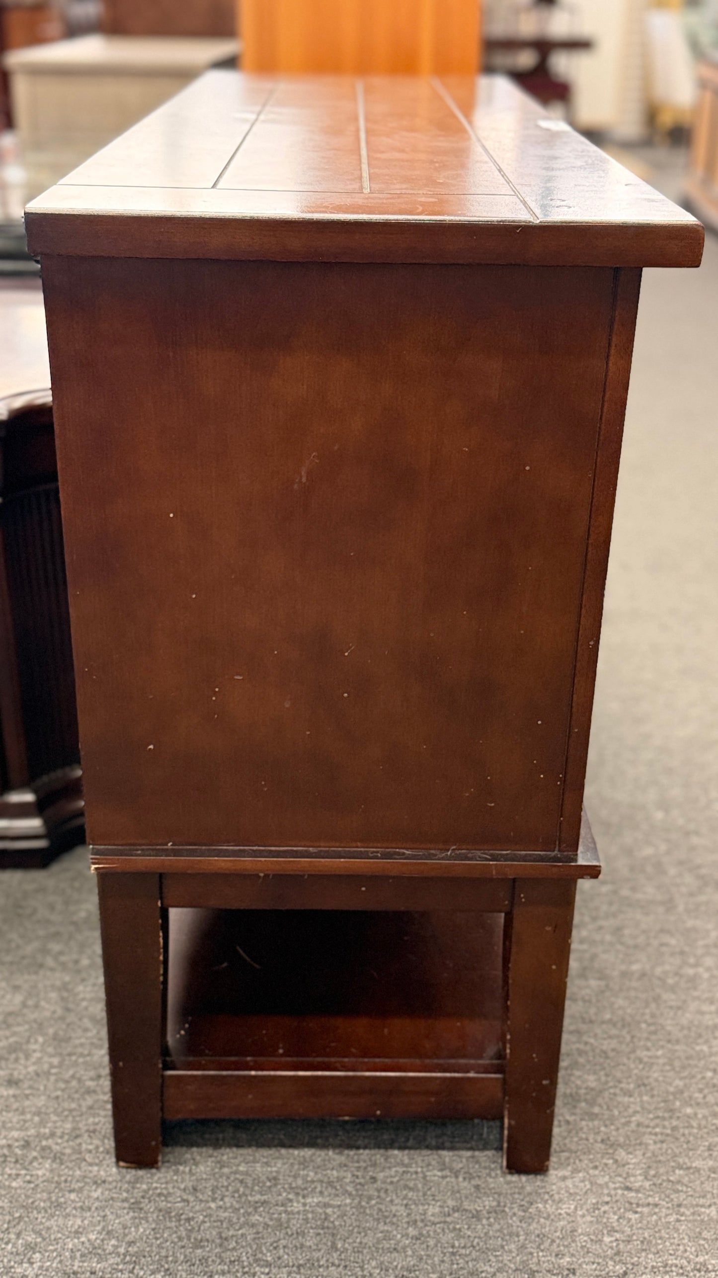 A medium-brown wooden console server featuring a central drawer, open center cubby, two louvered side doors, and a full-length lower display shelf.