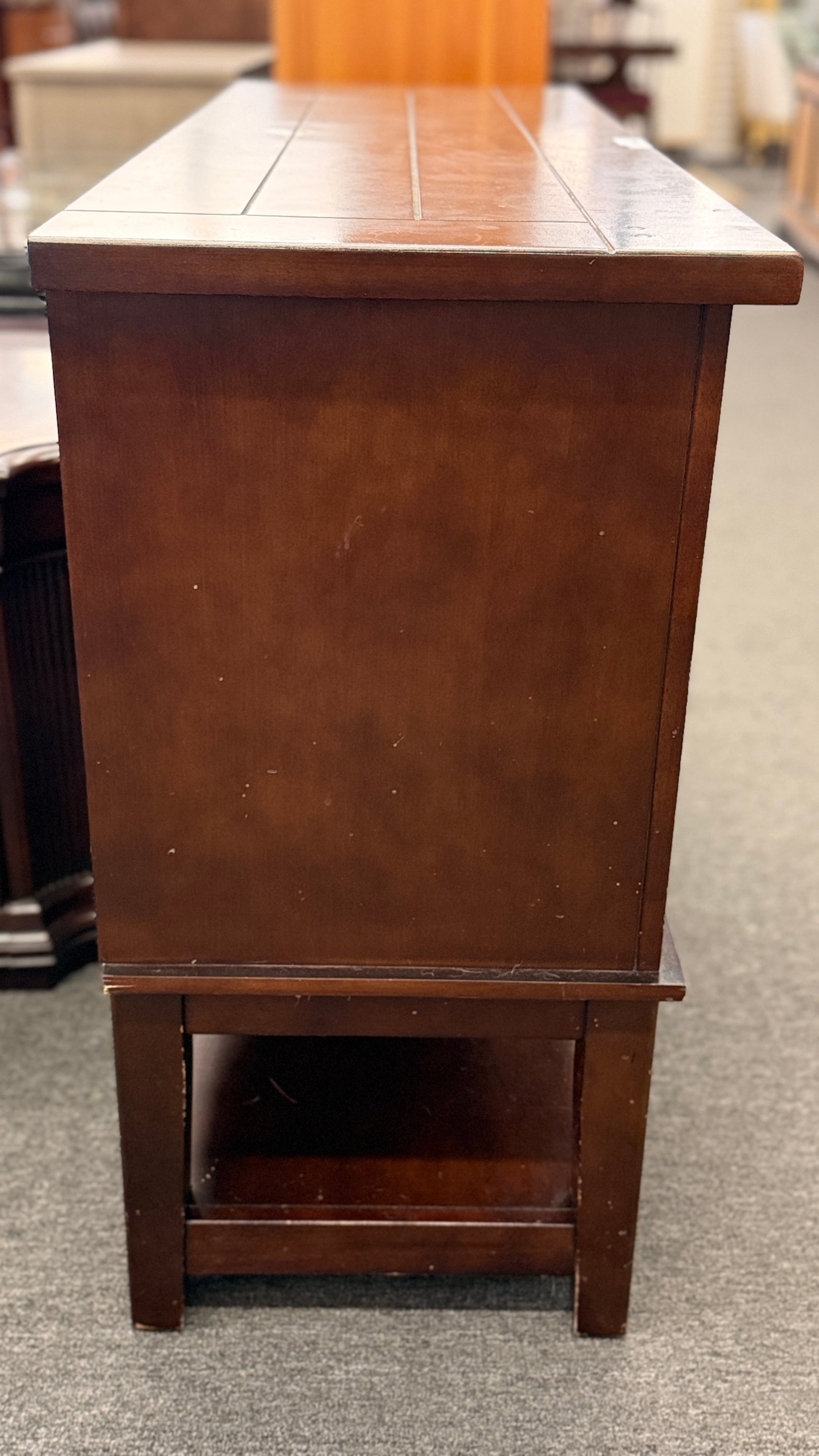 A medium-brown wooden console server featuring a central drawer, open center cubby, two louvered side doors, and a full-length lower display shelf.