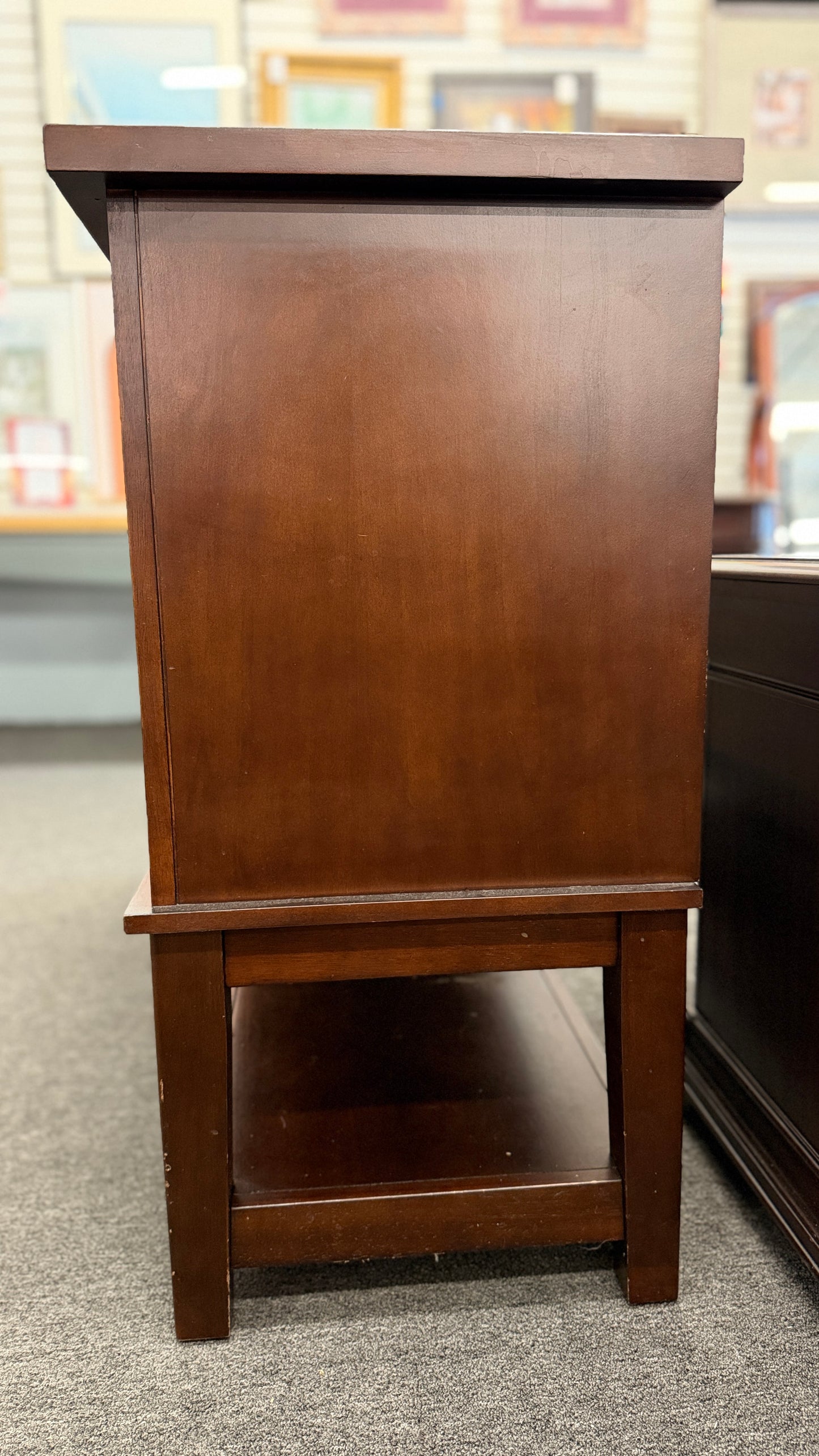 A medium-brown wooden console server featuring a central drawer, open center cubby, two louvered side doors, and a full-length lower display shelf.