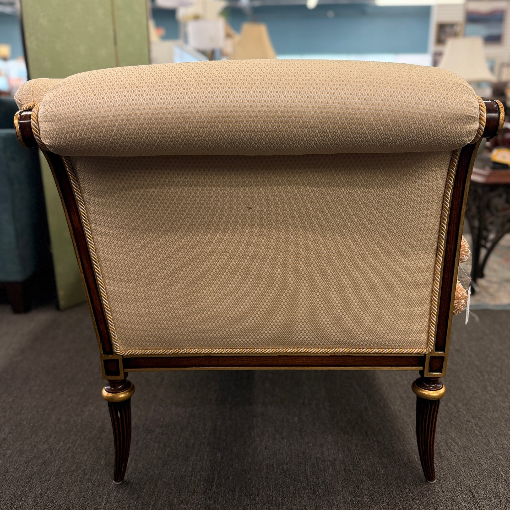 An elegant traditional cream upholstered settee loveseat featuring rolled arms, fringe trim along seat cushions, matching pillows, and fluted wooden legs.