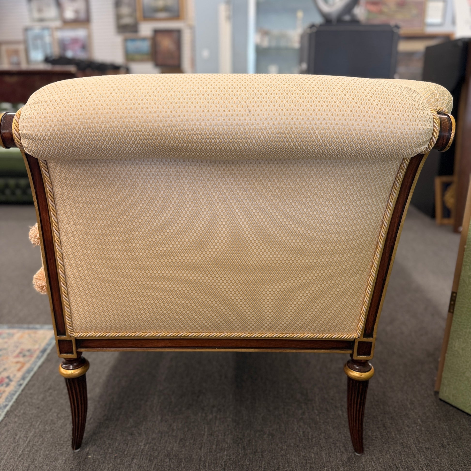 An elegant traditional cream upholstered settee loveseat featuring rolled arms, fringe trim along seat cushions, matching pillows, and fluted wooden legs.