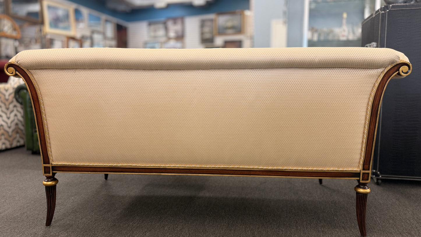An elegant traditional cream upholstered settee loveseat featuring rolled arms, fringe trim along seat cushions, matching pillows, and fluted wooden legs.