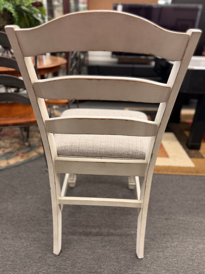 A two-tone counter-height dining set featuring a brown wood top rectangular table and six distressed white chairs with textured grey upholstered seats.