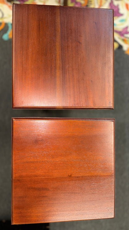 A pair of tall slim wooden side tables featuring square tops, lower display shelves, and cross-brace side details.