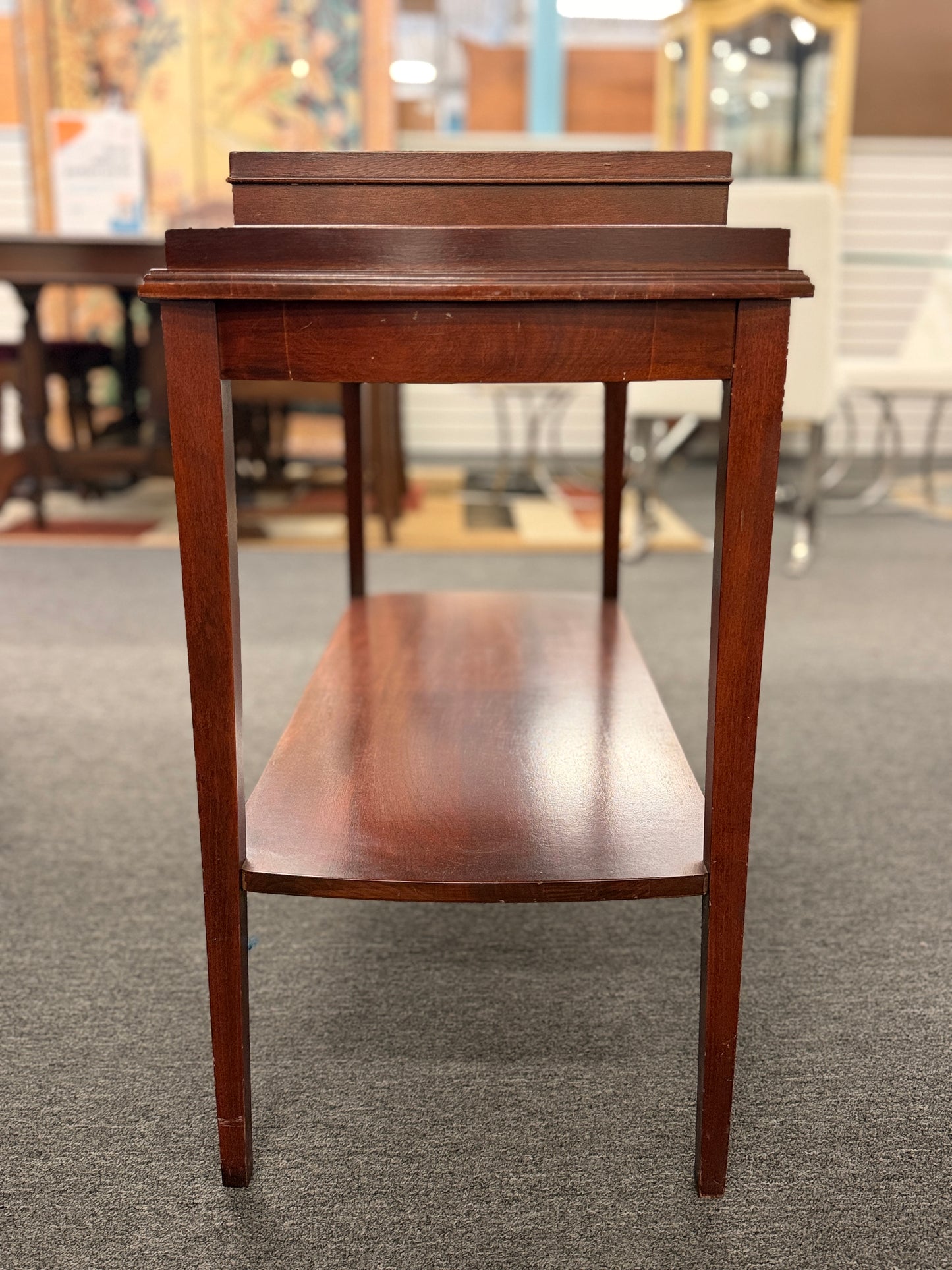 A classic mahogany-finished wooden console entry table featuring a center drawer with oval brass pull, tapered legs, and a lower shelf.