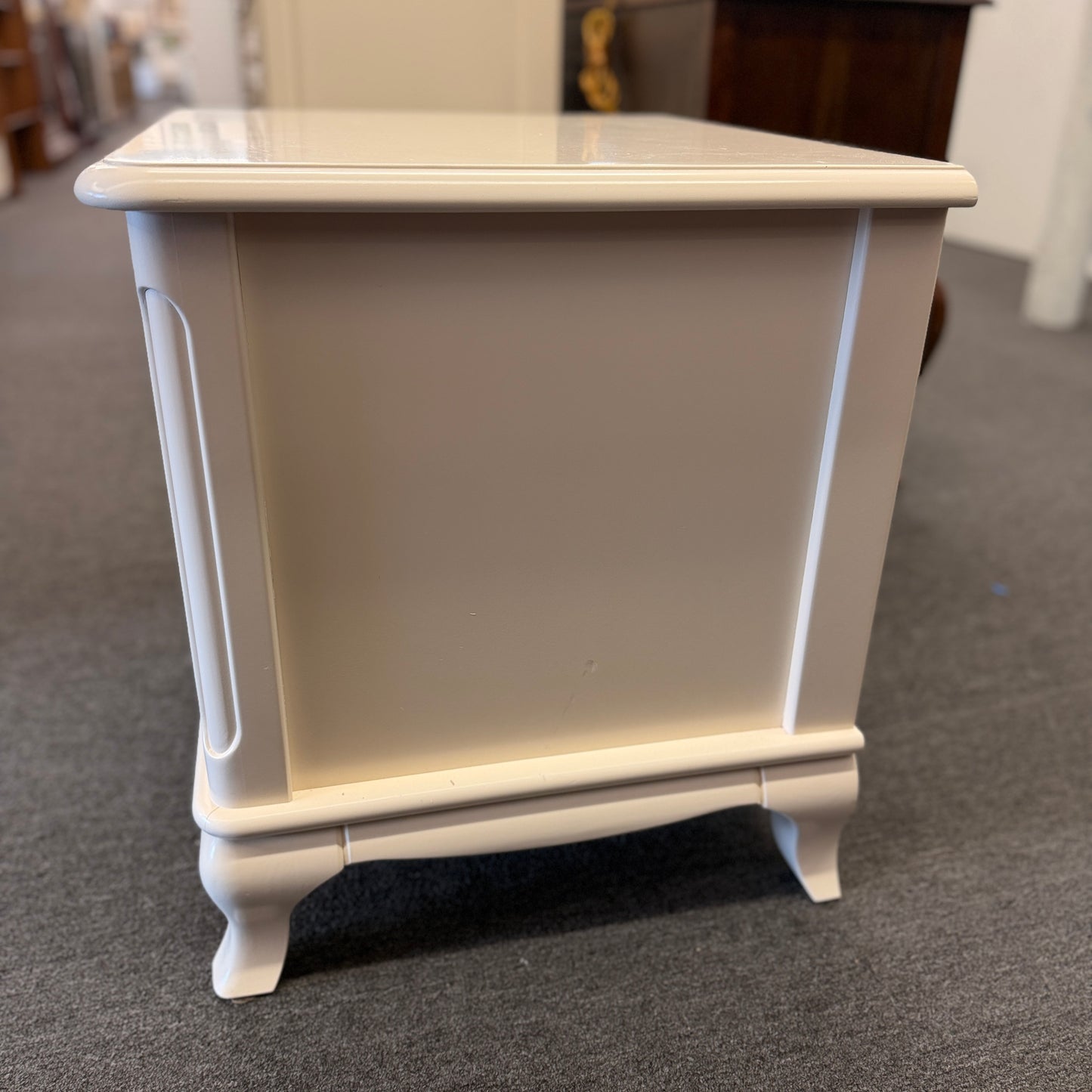 An off-white wooden nightstand featuring a single drawer with a turned knob, an open lower cubby, and curved cabriole legs.