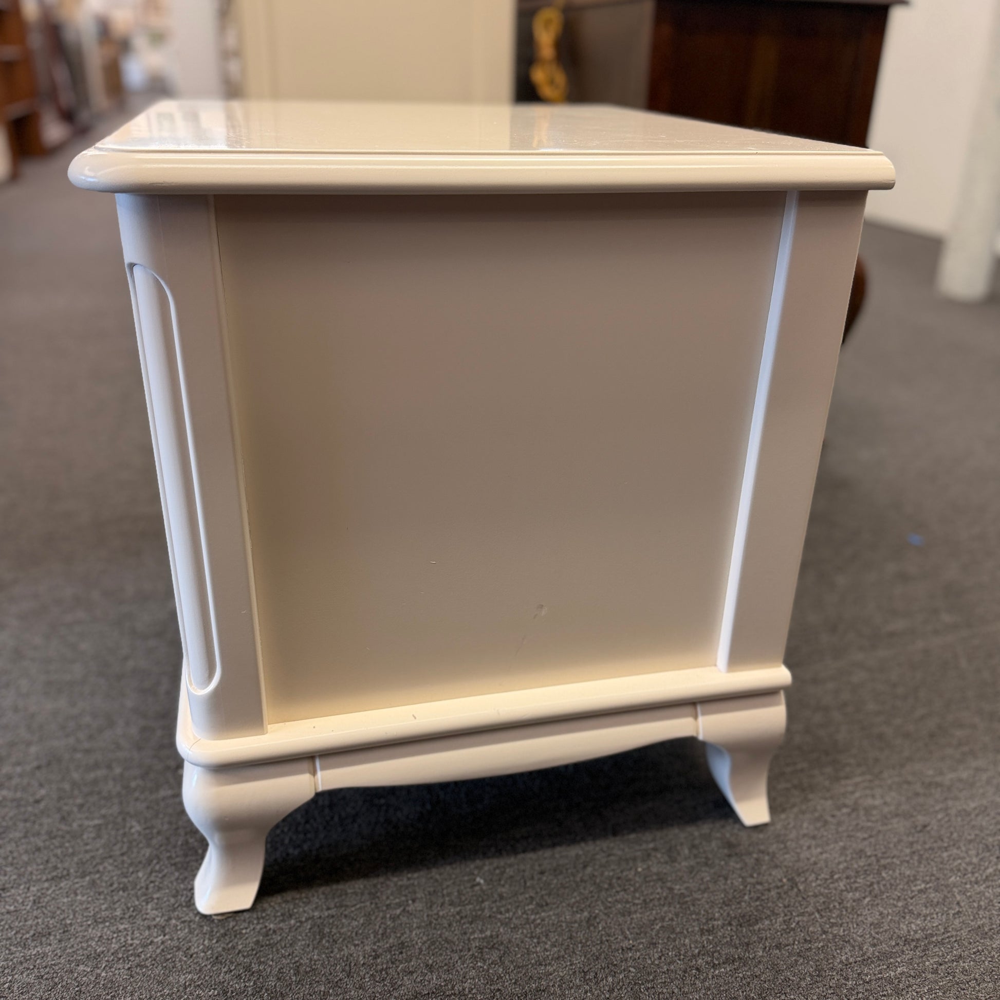 An off-white wooden nightstand featuring a single drawer with a turned knob, an open lower cubby, and curved cabriole legs.