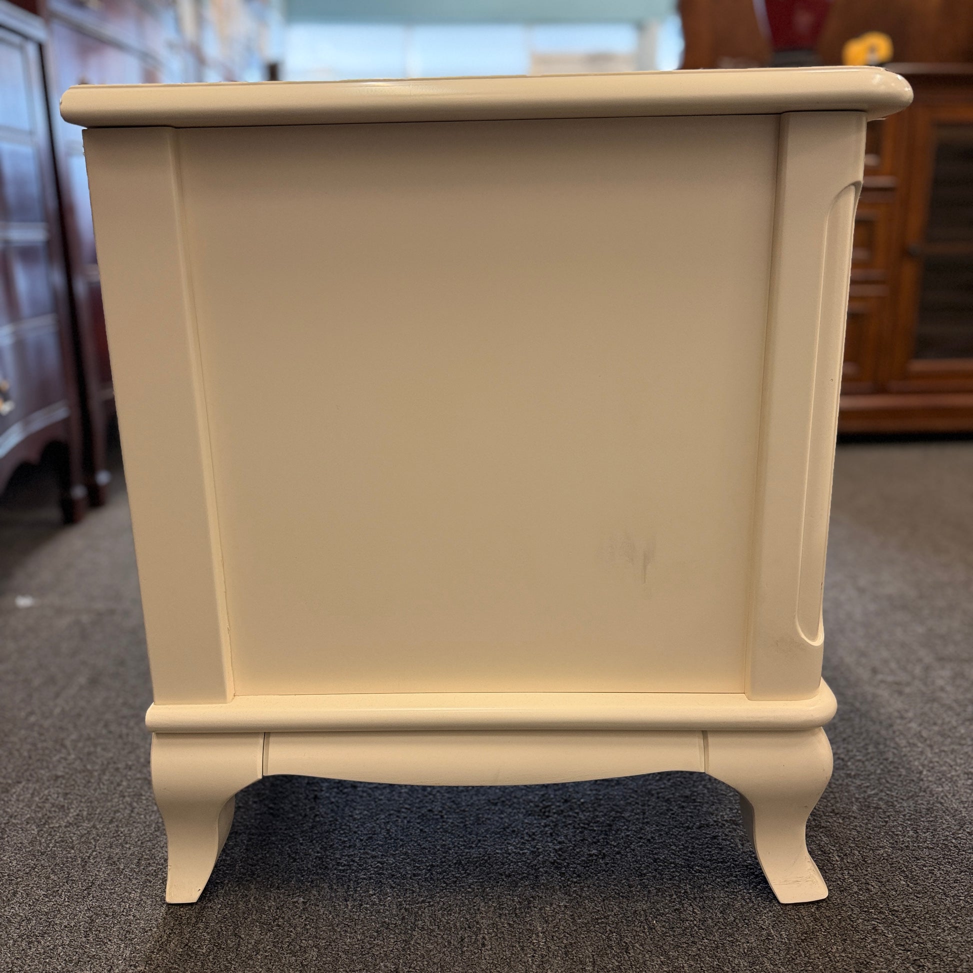 An off-white wooden nightstand featuring a single drawer with a turned knob, an open lower cubby, and curved cabriole legs.