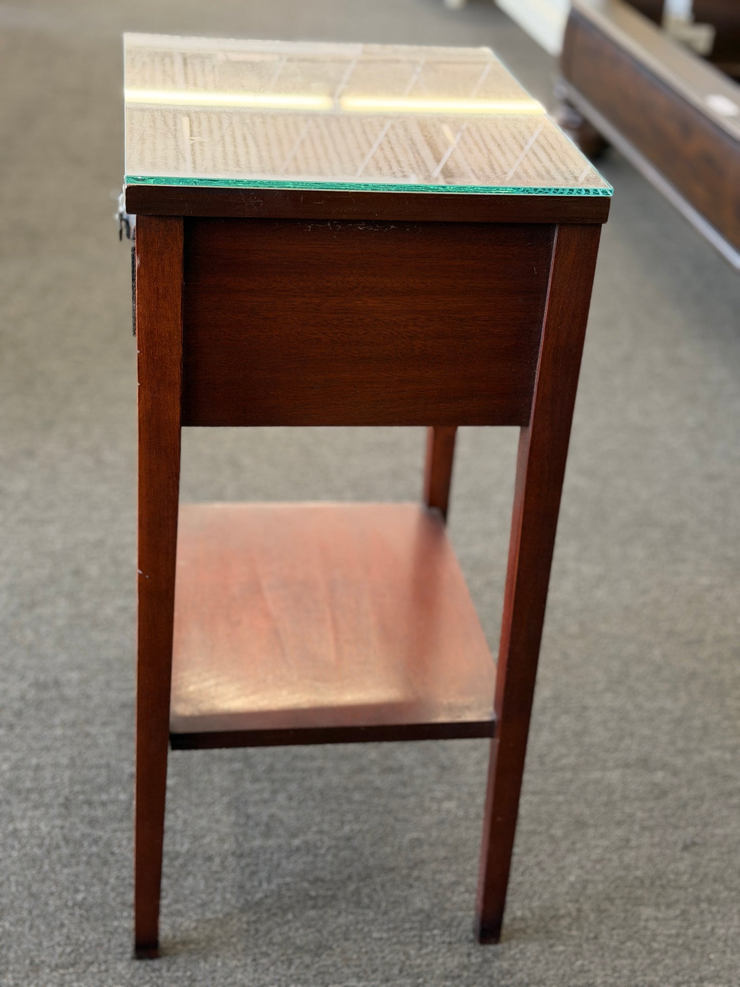 A Federal-style wood accent table featuring fluted corner accents, an arched apron, an oval rosette drop pull, an open lower shelf, and a glass top in good condition.