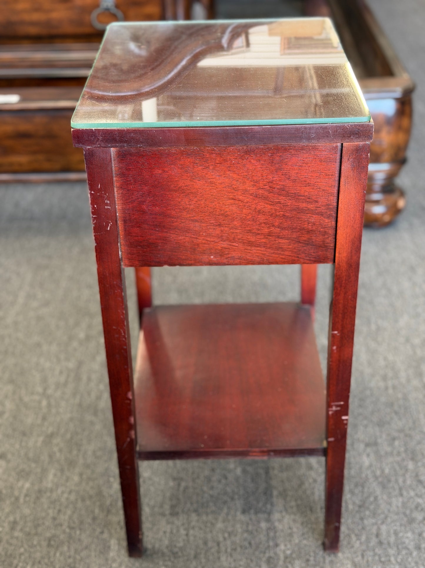 A compact Federal-style wood end table featuring fluted corner carvings, a single drawer with brass bail pull, lower shelf, and a custom glass top in good condition.