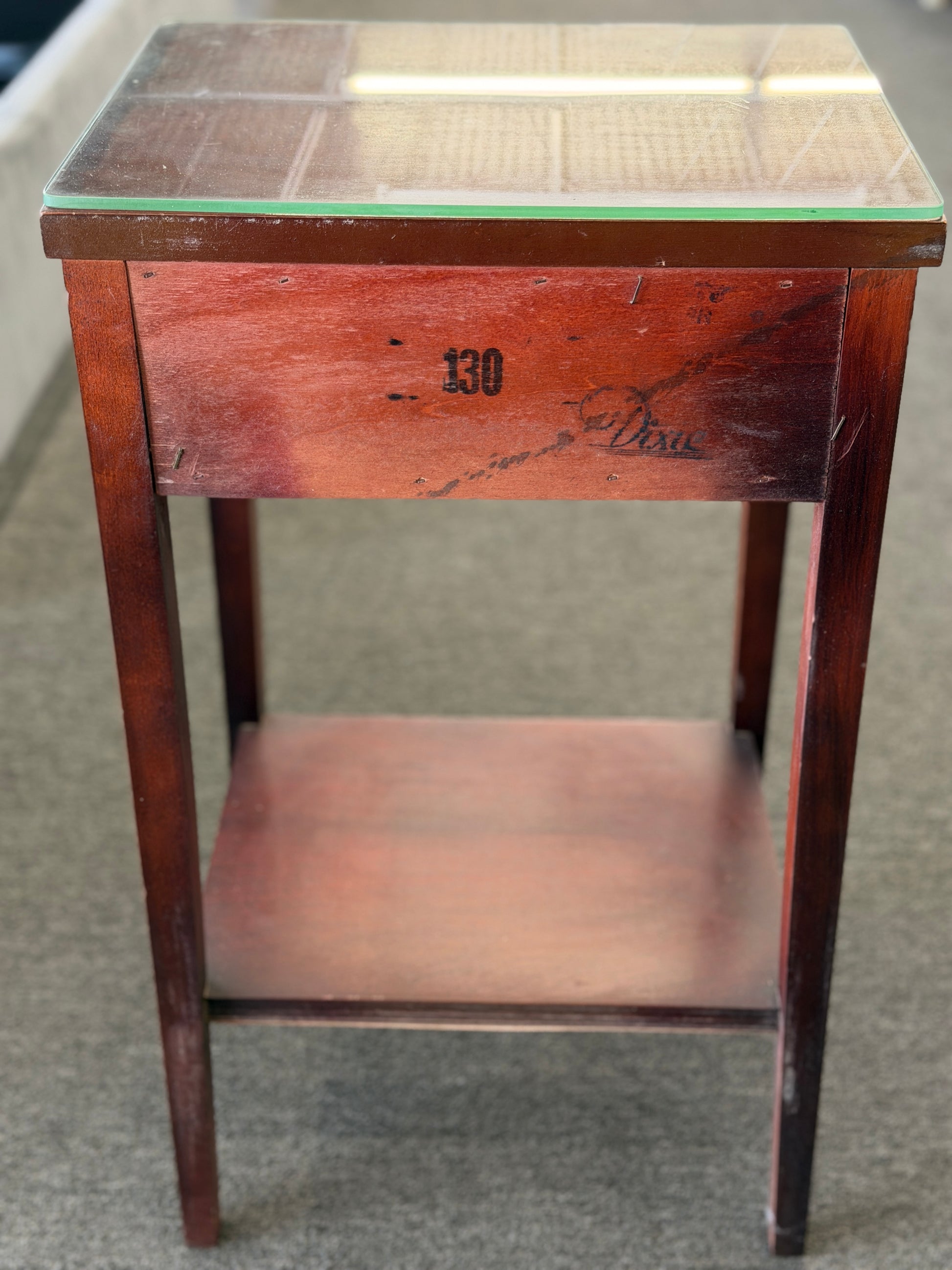 A compact Federal-style wood end table featuring fluted corner carvings, a single drawer with brass bail pull, lower shelf, and a custom glass top in good condition.