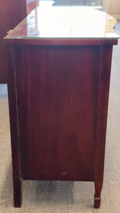 A vintage multi-drawer dresser in a rich reddish-brown wood finish with a serpentine front, brass handles, and a glass top in good condition.